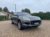 a grey porsche cayen is parked in a gravel parking lot
