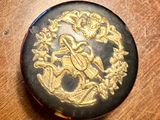 a black and gold button with a gold design on it