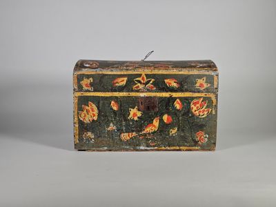une vieille malle ornée d'un motif floral est posée sur une surface blanche
