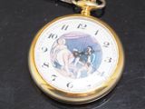 a gold pocket watch with a painting on it