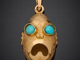 a close up of a gold pendant with a face with blue eyes