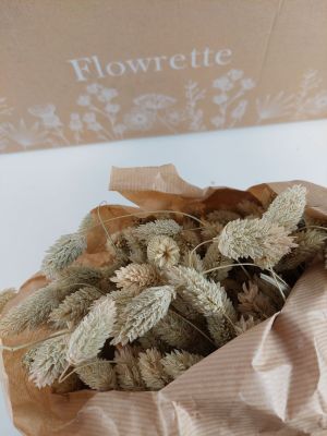 des fleurs séchées dans un sac en papier kraft posé sur une table blanche