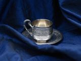 a silver cup and saucer sitting on a blue cloth