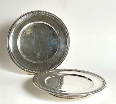 two silver plates sitting on a white surface