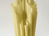 un vase blanc contenant du papier jaune, posé sur une surface blanche