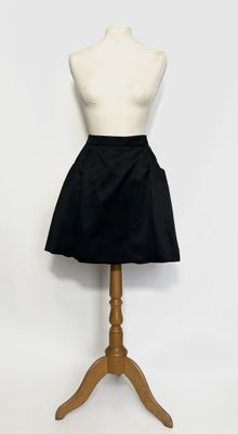 un mannequin vêtu d'une jupe noire, posé sur un socle en bois