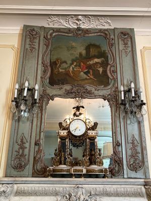 a clock on a mantle with a painting on the wall
