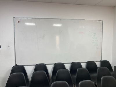 des rangées de chaises noires devant un tableau blanc dans une salle