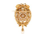 a close up of a gold broochle with a pearl drop