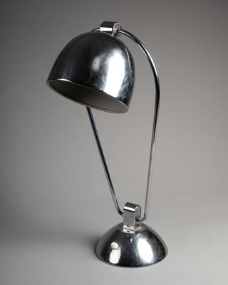 une photo d'une lampe de bureau argentée posée sur une surface blanche