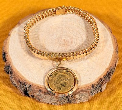 a close up of a gold bracelet with a coin on it
