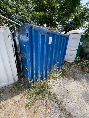 un conteneur bleu posé au milieu d'un champ de terre battue