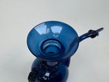 a blue glass vase with a handle on a table