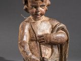 une vieille statue en bois représentant un enfant tenant un bâton