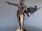 statue en bronze représentant un homme tenant un drapeau et désignant quelque chose du doigt