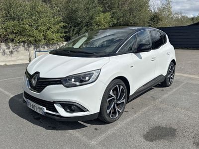 La voiture blanche est garée sur le parking, près des arbres.