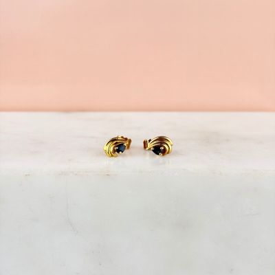 un gros plan sur une paire de boucles d'oreilles en or posées sur une surface en marbre