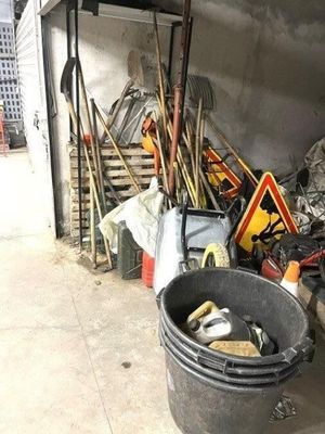 un seau rempli d'outils dans un garage, à côté d'un tas d'autres objets