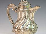 an antique silver coffee pot with a lid on a white surface