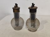une paire de bouteilles en verre anciennes avec des bouchons en métal, posées sur une table blanche