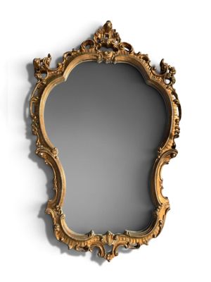 un miroir au cadre doré ouvragé accroché au mur, à côté d'un mur blanc