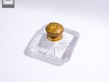 une petite boîte en verre avec un couvercle doré, posée sur une surface blanche