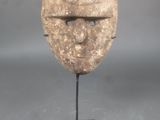 une image représentant un masque en pierre posé sur un socle, sur une surface grise