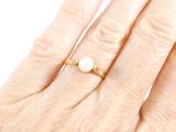 a woman ' s hand with a pearl ring on it