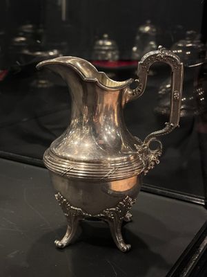 a silver pitcher that is on display in a glass case