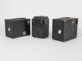three old cameras sitting side by side on a white surface