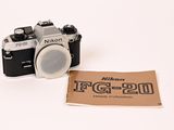 un petit appareil photo et une feuille de papier posée sur une surface blanche