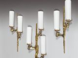 four brass wall sconces with white candles on them against a white wall