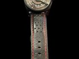 the watch has a black dial and red stitching on the strap