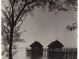 photographie en noir et blanc représentant deux cabanes situées au bord d'un plan d'eau