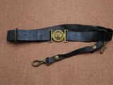 une ceinture en cuir noir avec une boucle en laiton sur fond marron