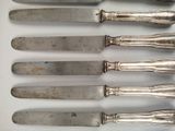 six silverplated knives are lined up in a row on a white surface