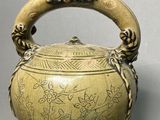 an old brass tea pot with a handle on a gray surface