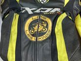 yellow and black leather motorcycle jacket on a bed with white sheets