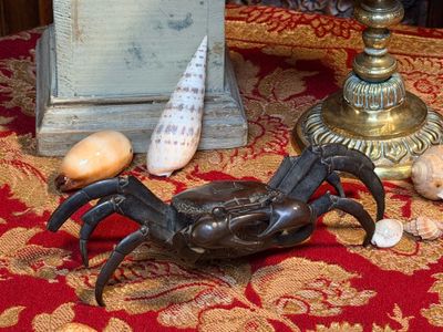 une statue représentant un crabe posé sur une table, à côté d'une horloge