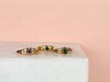 a close up of three gold rings with green and red stones on a marble block