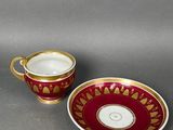 a red and gold cup and saucer on a grey surface