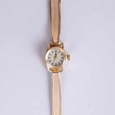 a gold wrist watch with a white face on a white surface