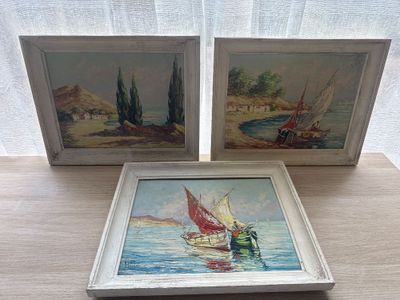 two framed paintings of boats on a wooden table next to a window