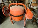 une bétonnière orange garée dans un garage, à côté d'une étagère remplie d'outils