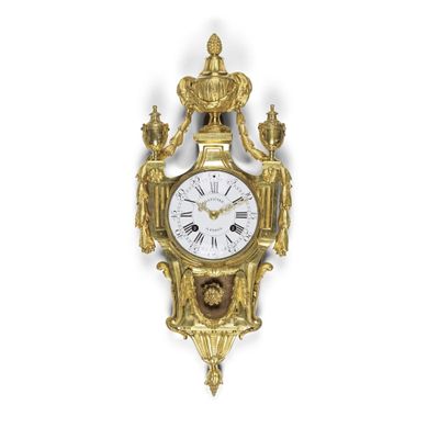 une horloge dorée accrochée à un mur blanc, sur laquelle est représentée une couronne