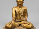 a gold statue of a seated buddha on a stone base