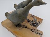 sculpture représentant deux canards perchés sur un bloc de bois posé sur une surface blanche