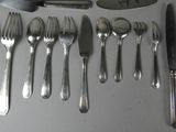 a lot of silverware on a table with a knife, spoon, and spoon rest