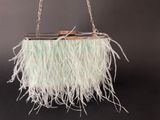a white purse with feathers hanging from a chain on a black background