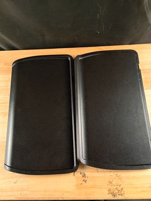 deux haut-parleurs noirs posés sur une table en bois, avec une chaise noire en arrière-plan